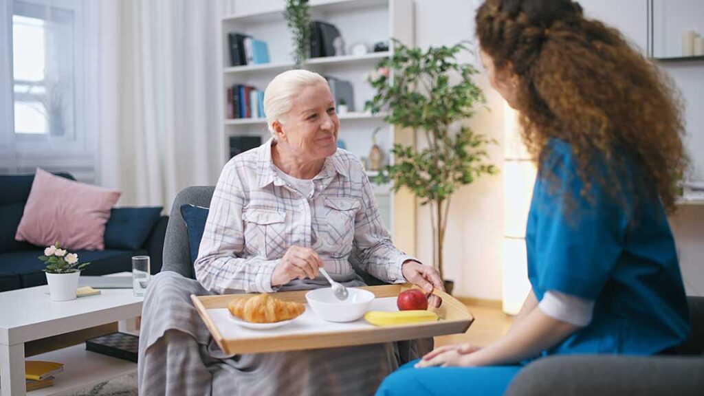 An older adult sits with a younger family member at a kitchen table, talking and looking at photo albums together.