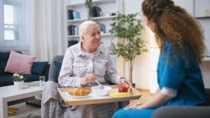 An older adult sits with a younger family member at a kitchen table, talking and looking at photo albums together.