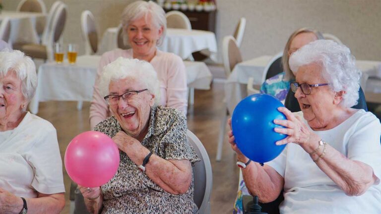 A social worker speaks with an older resident and family member at a quiet assisted living table.